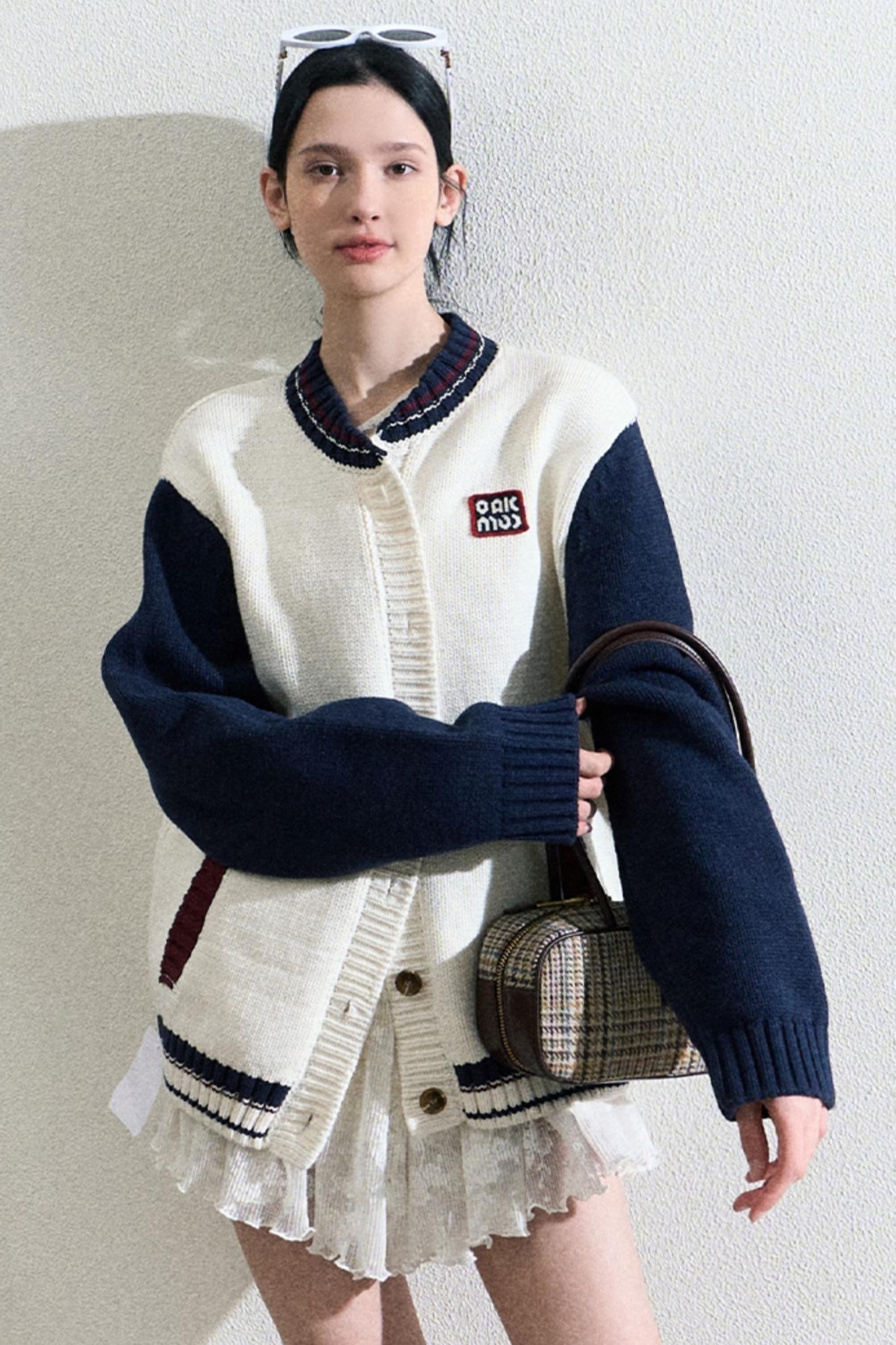 A woman wearing a Varsity-Style Cardigan with white and navy colors, featuring a varsity logo on the chest.