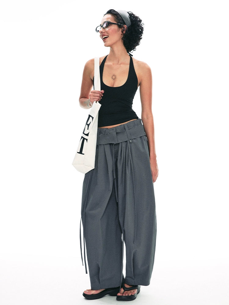 Woman wearing a black tank top and gray wide-leg pants, holding a white tote bag with text.