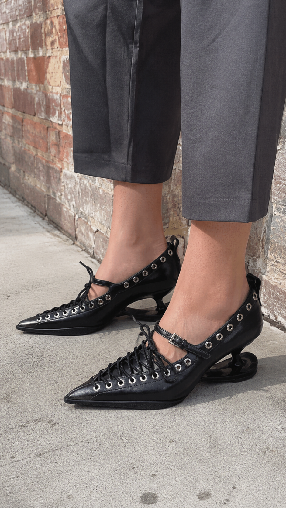 Black Corset-Lace Pointed Stiletto Pumps — Neighborhood pavement — side view; AI-generated lifestyle showcase