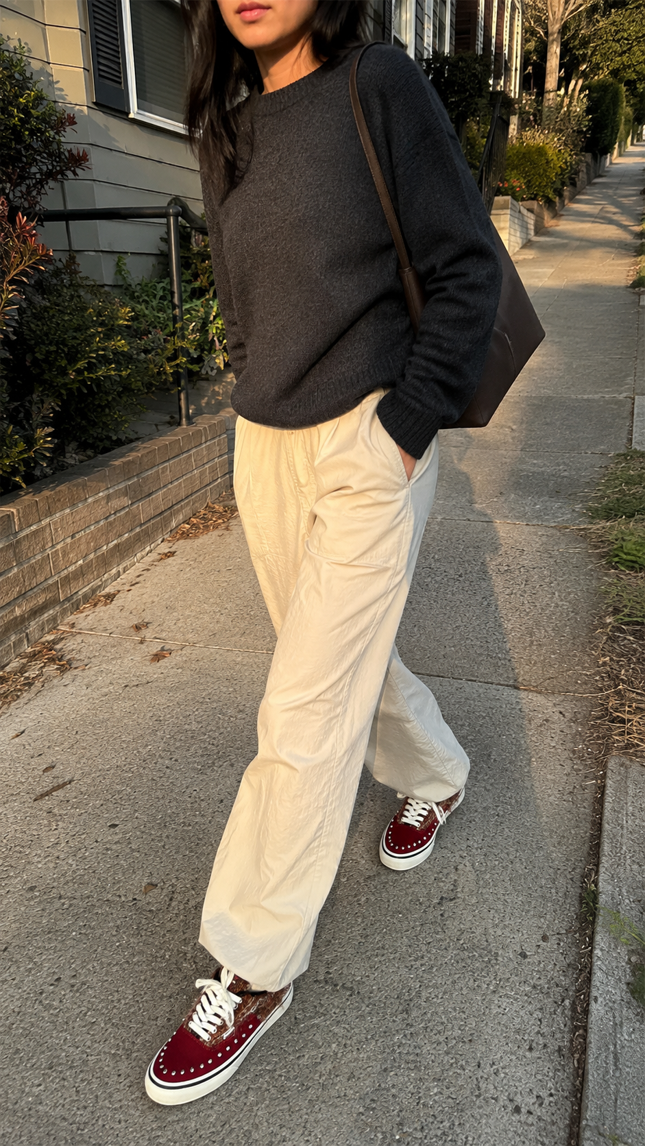 Reddish-brown studded suede low-top sneakers worn on a neighborhood sidewalk