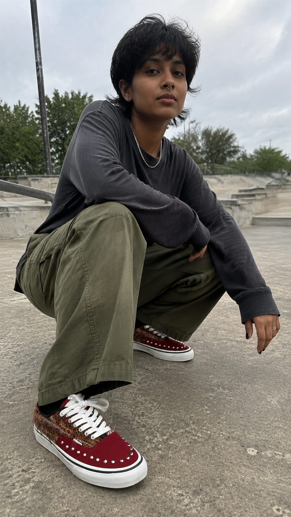 Reddish-brown studded suede low-top sneakers at a concrete skate plaza